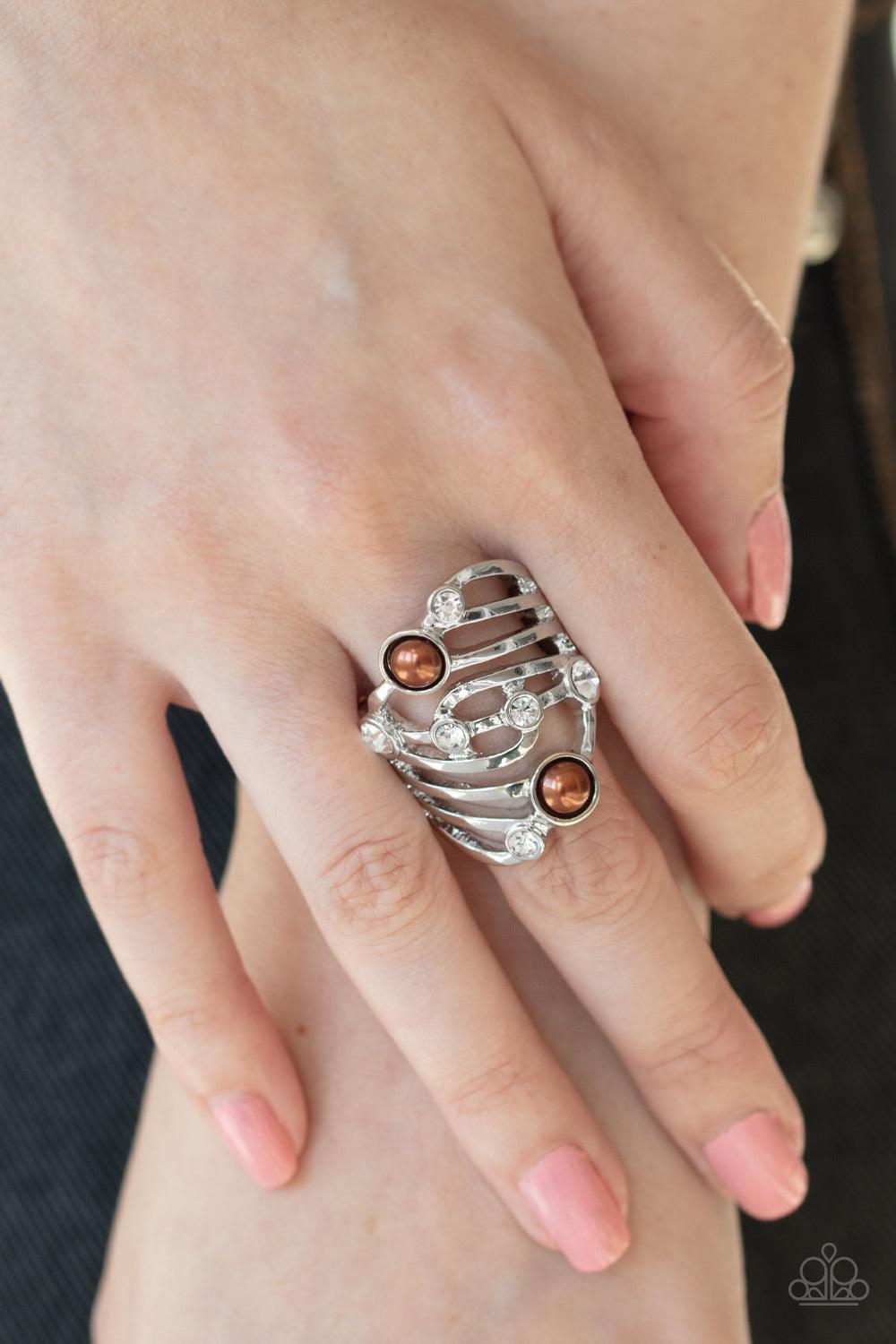 Paparazzi Accessories Dancing Diamonds - Brown Dotted in glassy white rhinestones and dainty brown pearls, whirling silver bands stack across the finger for a refined layered look. Features a stretchy band for a flexible fit. Jewelry