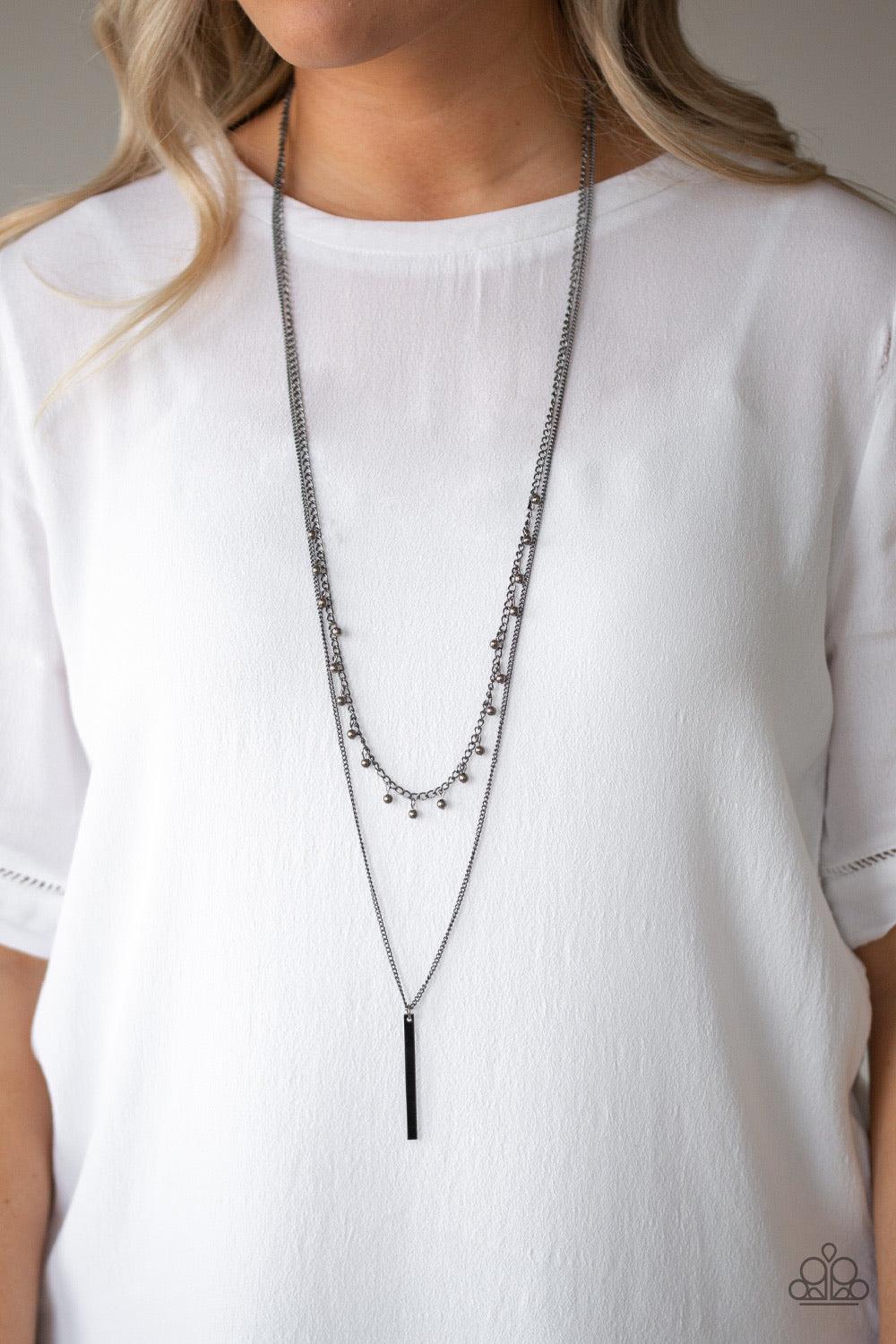 Paparazzi Accessories Keep Your Eye On The Pendulum - Black Two mismatched gunmetal chains layer down the chest. Dainty gunmetal beads dangle from the bottom of the uppermost chain, while a rectangular pendulum-like pendant swings from the lowermost chain