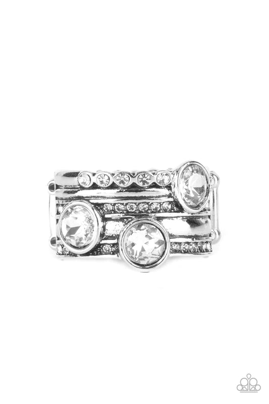 Paparazzi Accessories Pack It On - White A trio of oversized white rhinestones haphazardly adorns layers of mismatched rows of dainty white rhinestones and antiqued silver bands, coalescing into a knockout centerpiece. Features a stretchy band for a flexi