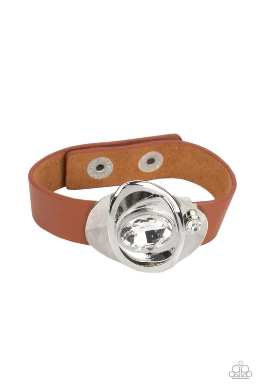 Paparazzi Accessories Pasadena Prairies - Brown Embellished with an oversized white oval gem, asymmetrical silver frames haphazardly stack into an abstract floral-inspired centerpiece. A smaller white rhinestone attaches the metallic structure to a band o