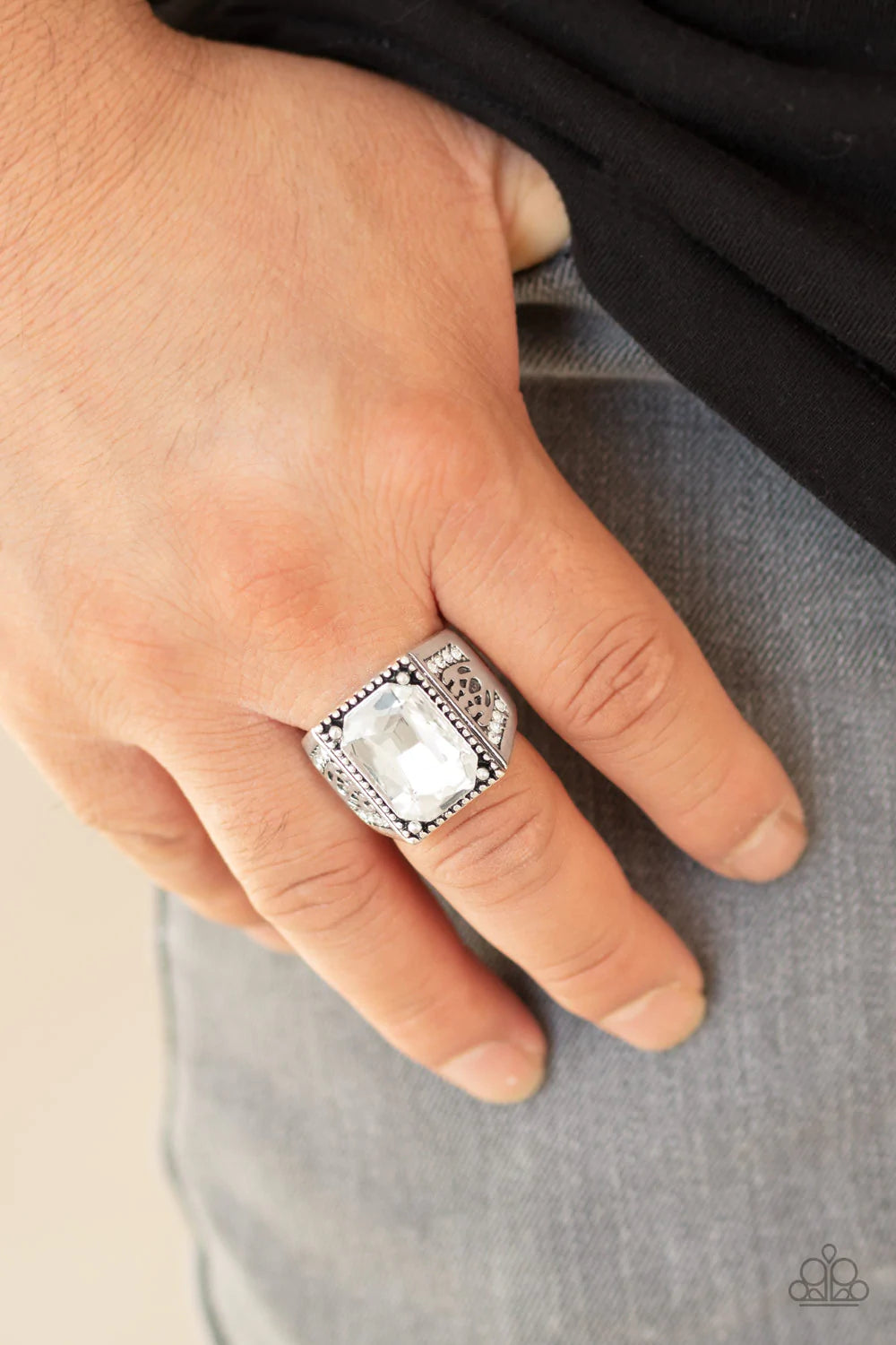 Paparazzi Accessories Conquered - White Featuring an emerald style cut, a white gem is pressed into the center of a studded silver frame featuring an ornate silver band encrusted in sections of white rhinestones. Features a stretchy band for a flexible fi