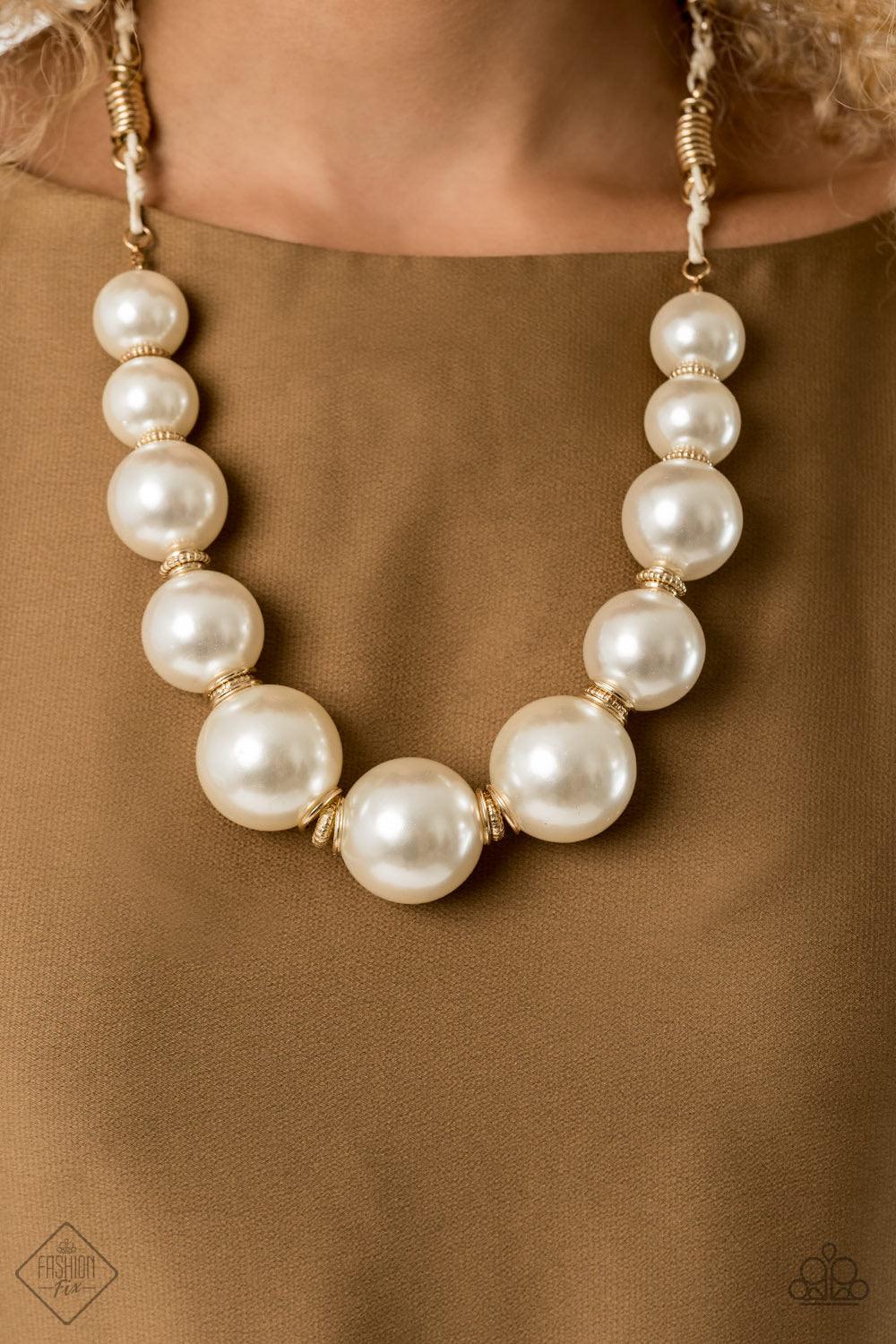 Paparazzi Accessories Pearly Prosperity - Gold Separated by stacks of smooth and decorative gold rings, a collection of dramatically oversized white pearls are delicately hand-strung along an invisible wire that attaches to knotted strands of white cordin