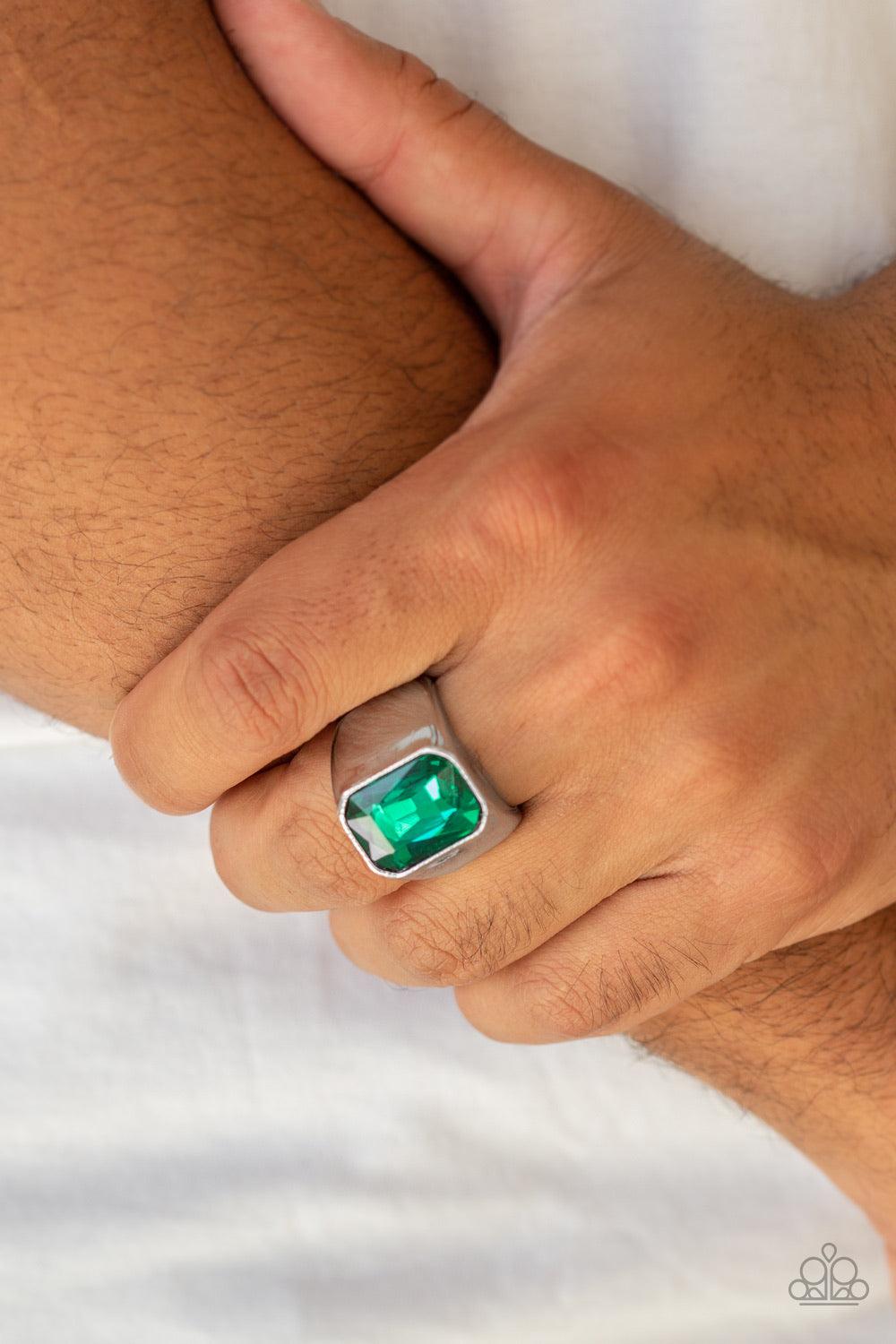 Paparazzi Accessories Scholar - Green Featuring a kingly emerald style cut, an oversized green rhinestone is pressed into the center of a glistening silver band for a statement look. Features a stretchy band for a flexible fit. Jewelry
