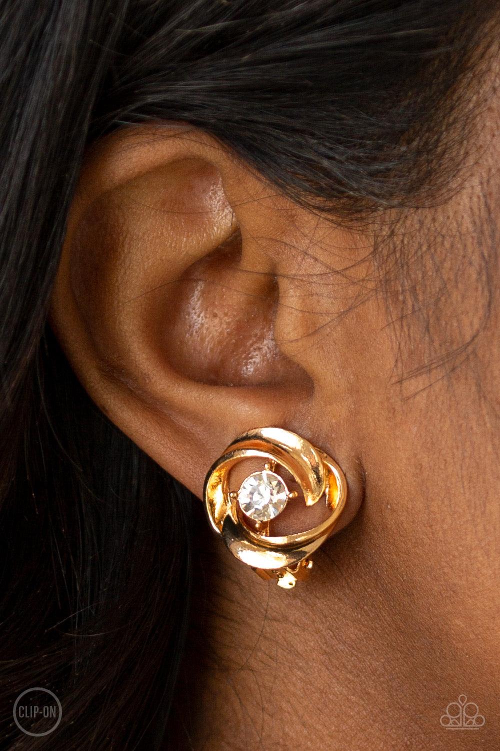 Paparazzi Accessories Girl Whirl - Gold *Clip-On Glistening gold ribbons whirl around a dainty white rhinestone center, coalescing into a refined frame. Earring attaches to a standard clip-on fitting. Jewelry