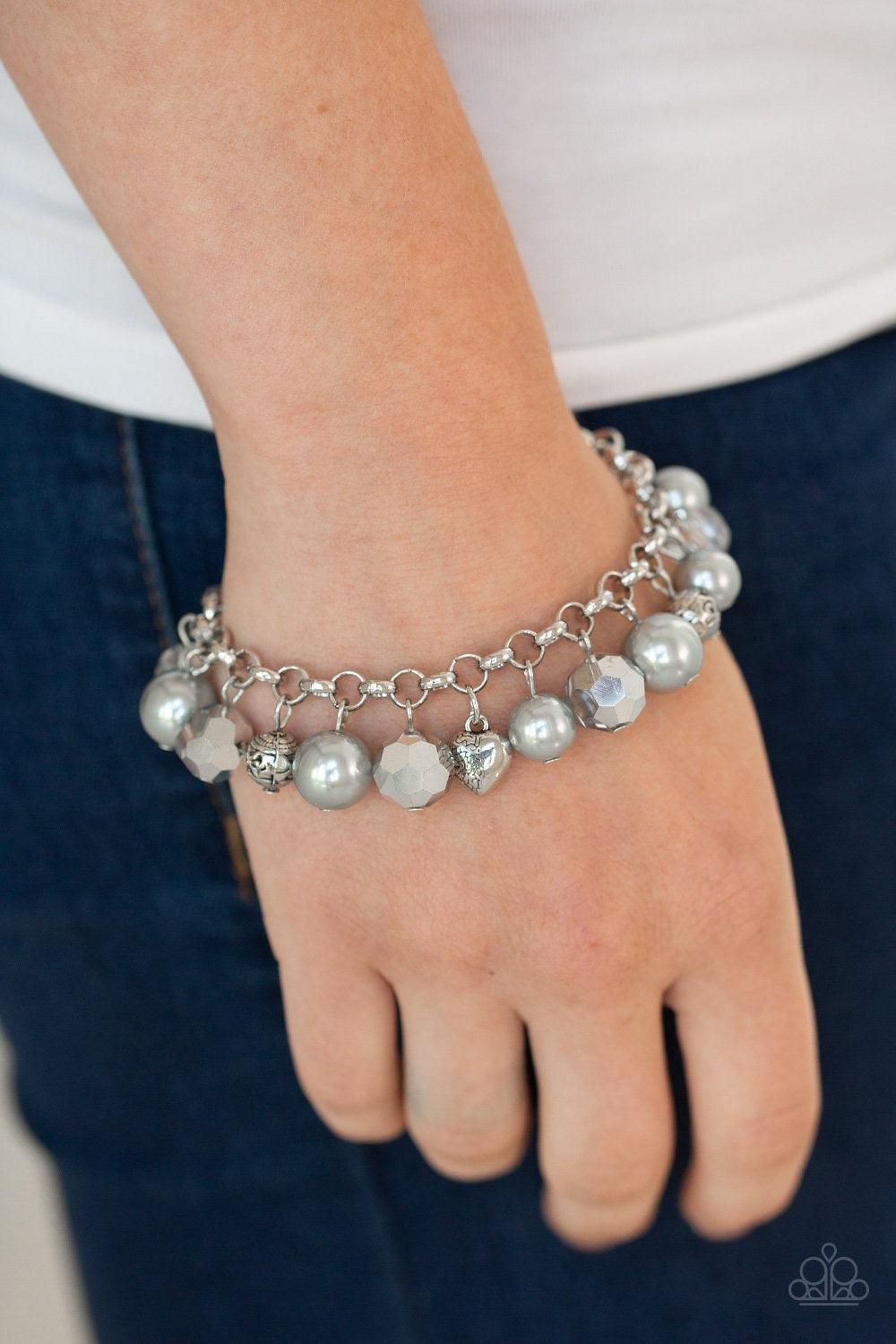 Paparazzi Accessories Cupid Couture - Silver Featuring a dainty silver heart charm, rose charm, and ornate silver beads, a refined collection of white pearls and metallic crystal-like beads swing from the wrist for a flirtatious flair. Features an adjusta