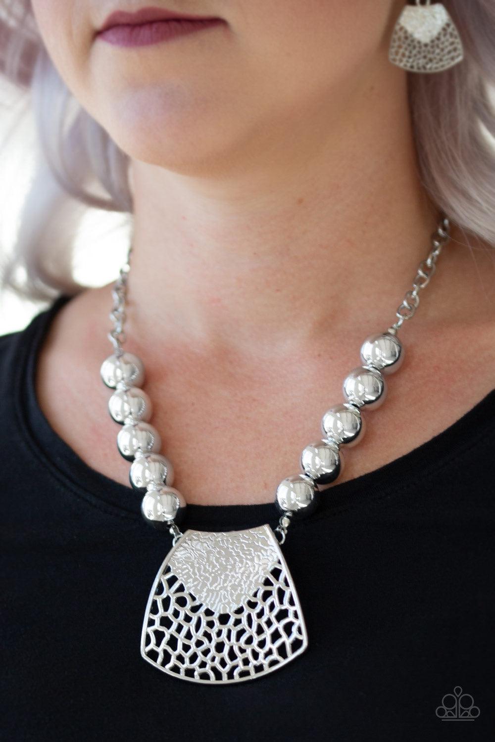 Paparazzi Accessories Large And In Charge - Silver Featuring ornately stenciled and embossed details, a flared silver plate swings from a boldly silver beaded chain below the collar for a fierce look. Features an adjustable clasp closure. Jewelry