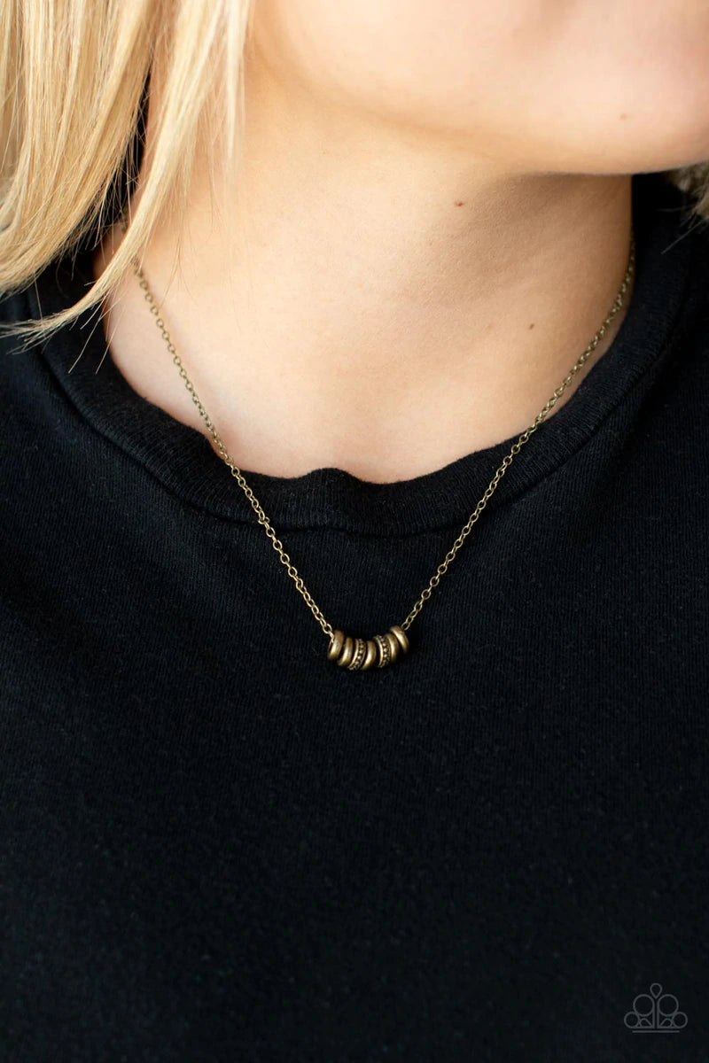 Paparazzi Accessories Dainty Dalliance - Brass An antiqued collection of smooth and studded brass rings glide along a dainty brass chain below the collar, creating a minimalist inspired look. Features an adjustable clasp closure. Sold as one individual ne