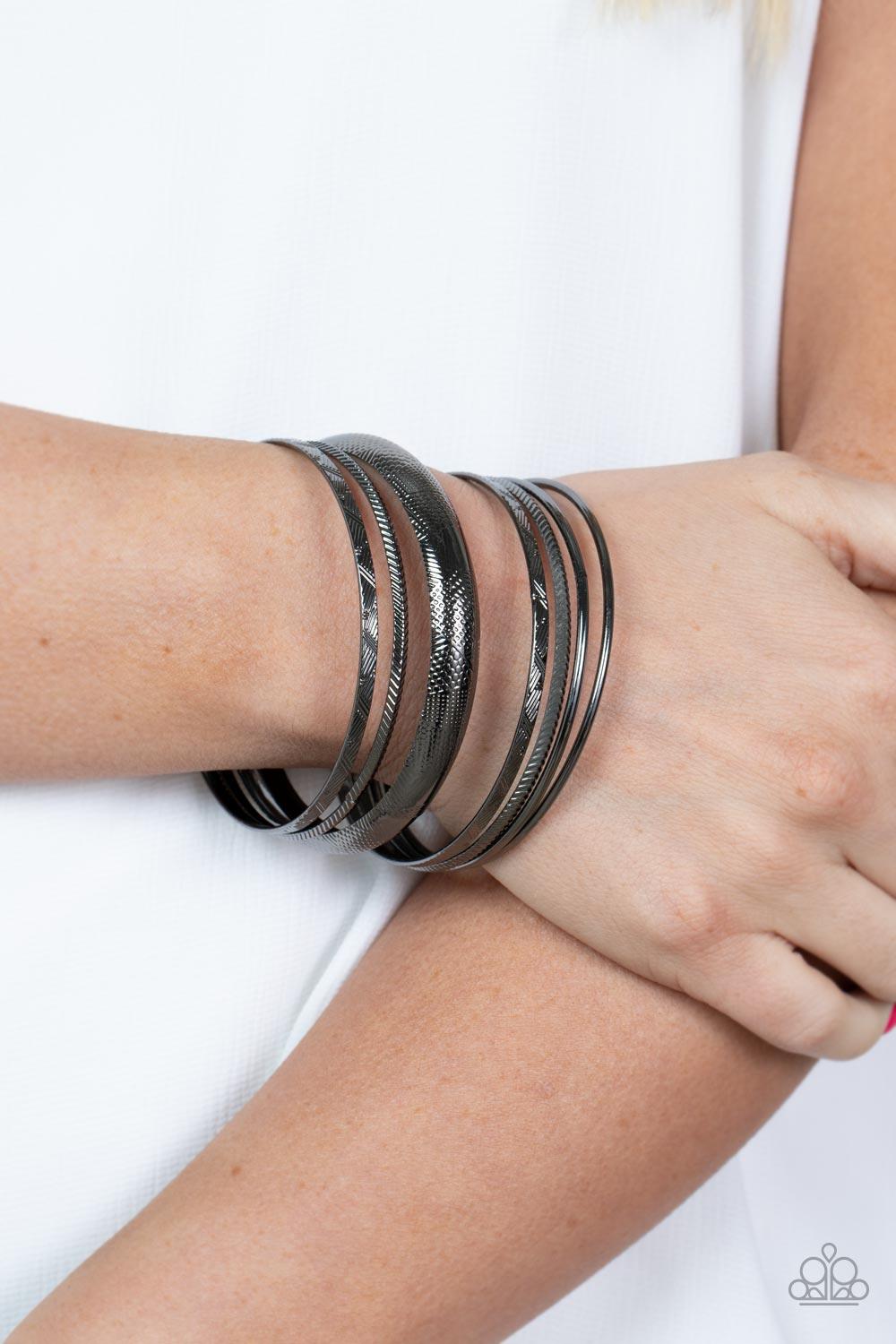Paparazzi Accessories Stackable Stunner - Black A jangling symphony of classic gunmetal bangles featuring shiny and textured finishes and varying sizes stack up the wrist for a layered look. Sold as one set of seven bracelets. Jewelry
