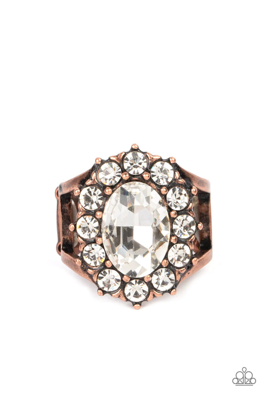 Paparazzi Accessories Moxie Magic A dauntless oval rhinestone is encircled by dainty sparkling gems. Accented with petite antiqued copper studs, the dramatic design joins with an airy layered copper band to create a captivating arrangement atop the finger