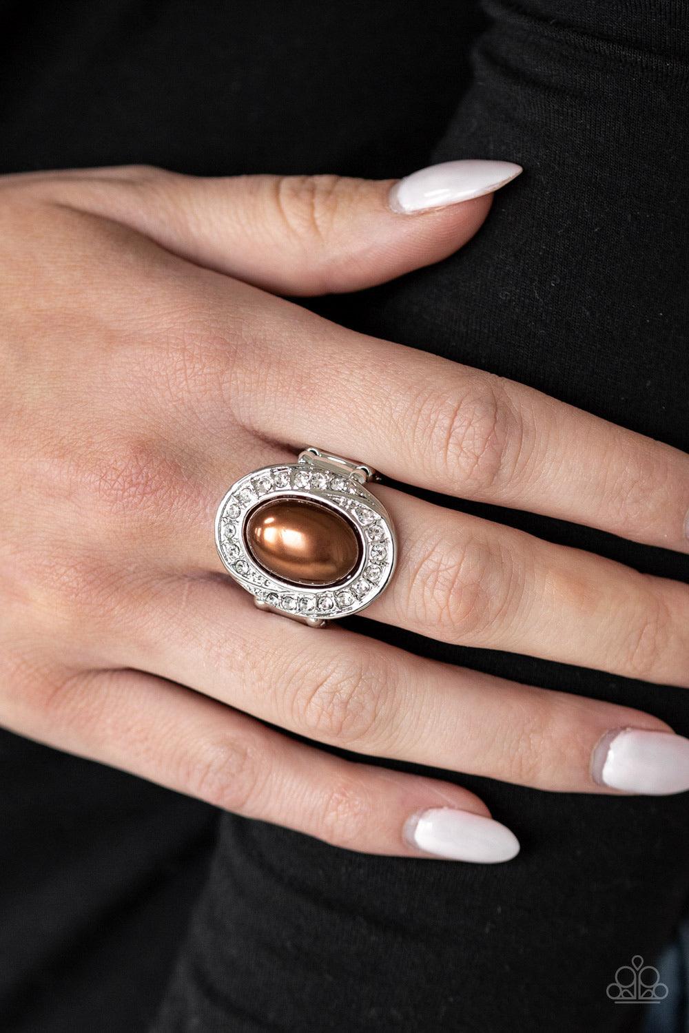 Paparazzi Accessories The ROYALE Treatment - Brown A pearly brown bead is pressed into a silver oval frame radiating with a ring of glittery white rhinestones, creating a regal statement piece atop the finger. Features a stretchy band for a flexible fit.