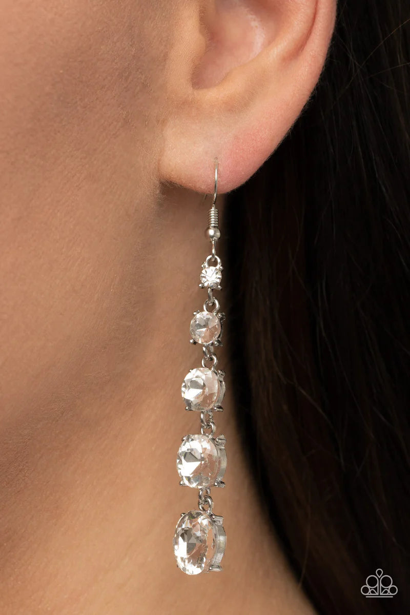 Paparazzi Accessories Red Carpet Charmer - White Encased in pronged silver fittings, a dramatic display of glittery white rhinestones gradually increase in size as they trickle from the ear for a timeless look. Earring attaches to a standard fishhook fitt