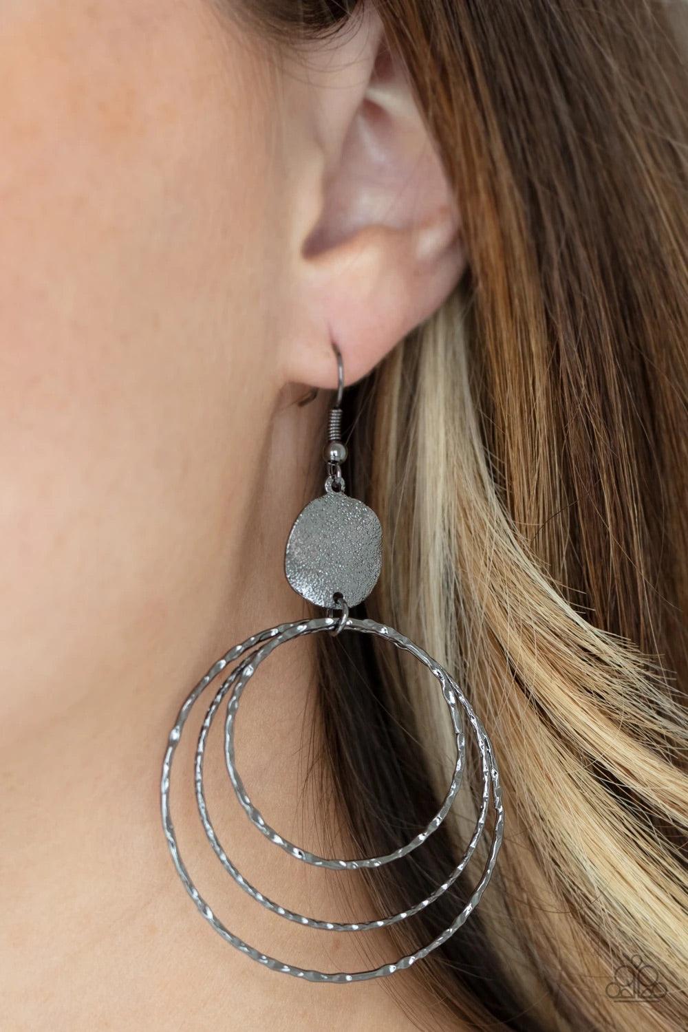Paparazzi Accessories Universal Rehearsal ~Black A shimmery wavy gunmetal disc links atop a collection of three delicately hammered gunmetal rings in concentric sizes for an out-of-this-world finish. Earring attaches to a standard fishhook fitting. Sold a
