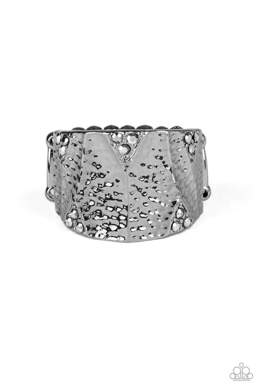 Paparazzi Accessories Industrial Indentation - Black Featuring clusters of dainty hematite rhinestones, a thick hammered gunmetal band is shaved into an uneven frame for an edgy shimmer. Features a stretchy band for a flexible fit. Sold as one individual