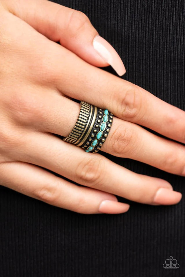 Paparazzi Accessories Local Flavor - Brass A wide brass band is overlaid with layers of linear texture, smooth brass bars, and antiqued studs. A row of dainty oval shaped turquoise stones flows across the band, adding a splash of color atop the finger. Fe