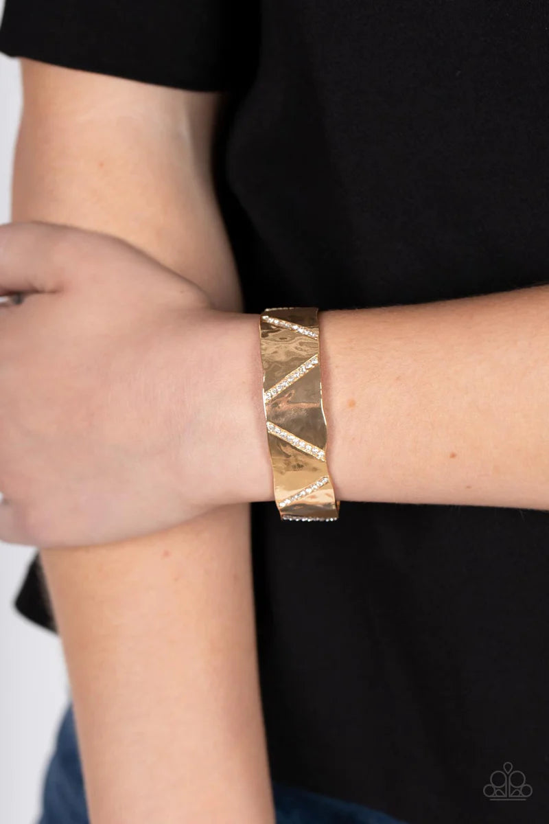 Paparazzi Accessories Couture Crusher - Gold Rows of glassy white rhinestones slant across the front of a gently hammered gold cuff that waves around the wrist, result in an edgy shimmer. Sold as one individual bracelet.