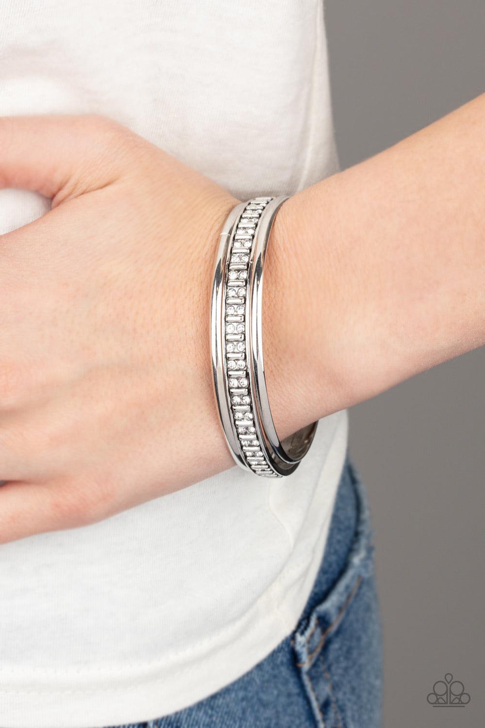 Paparazzi Accessories Flawless Flaunter - White Two classic silver bangles join a thick silver bangle that has been encrusted in pairs of dainty white rhinestones and rectangular silver beading for an edgy refinement. Jewelry