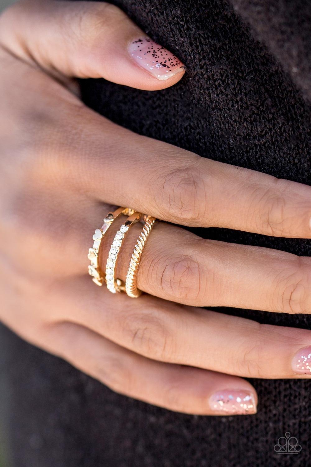 Paparazzi Accessories Dear To My Heart - Gold Three glistening gold bands arc across the finger. Dainty heart accents are pressed into the uppermost band, while glittery white rhinestones are encrusted along the centermost band and shimmery serrated textu