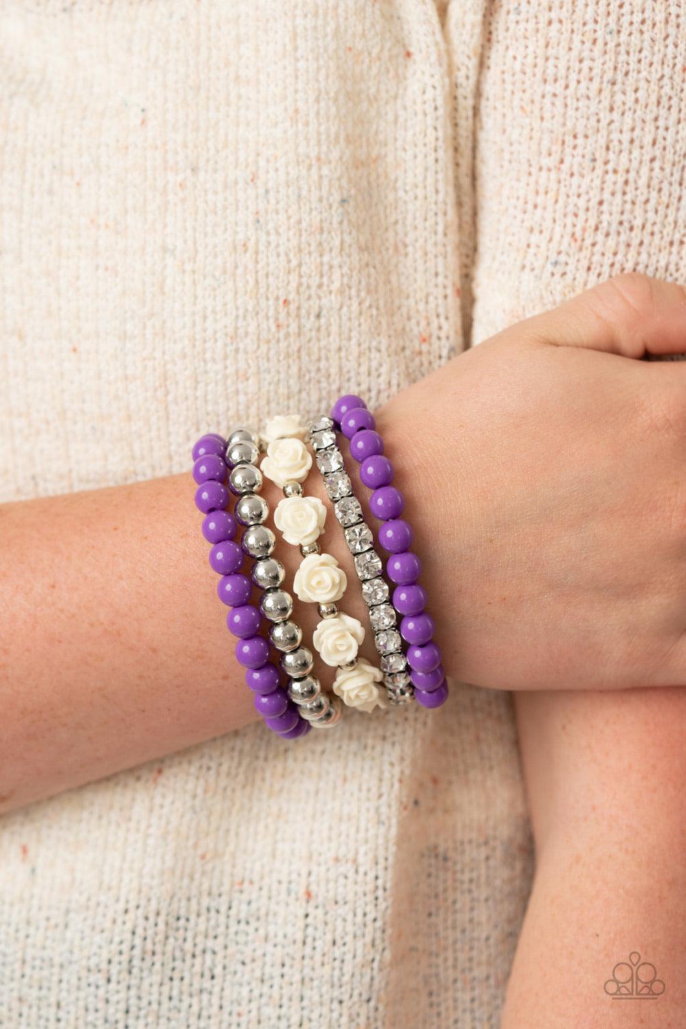 Paparazzi Accessories Rose Garden Grandeur - Purple A vintage inspired collection of white resin roses, purple beads, and classic silver beads join a stretchy band of glittery white rhinestones dotted around the wrist for a flawlessly stacked look. Sold a