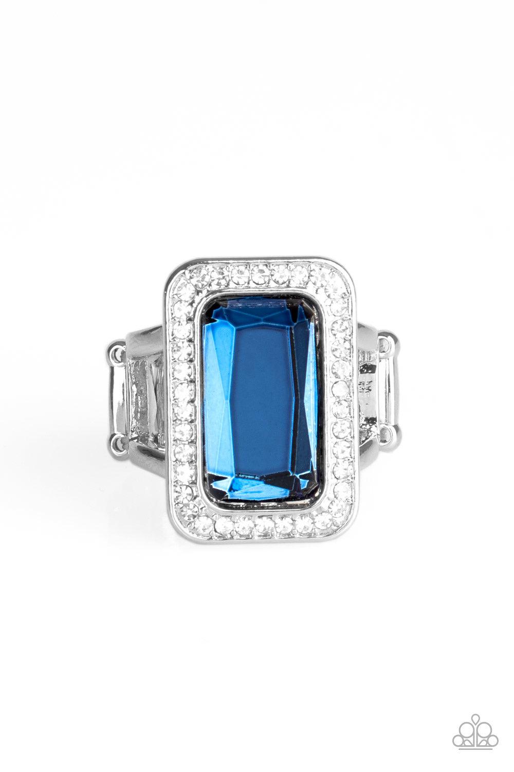 Paparazzi Accessories Crown Jewel Jubilee - Blue Featuring a regal emerald style cut, an oversized blue gem is bordered by a silver frame encrusted in glassy white rhinestones for a glamorous look. Features a stretchy band for a flexible fit Jewelry