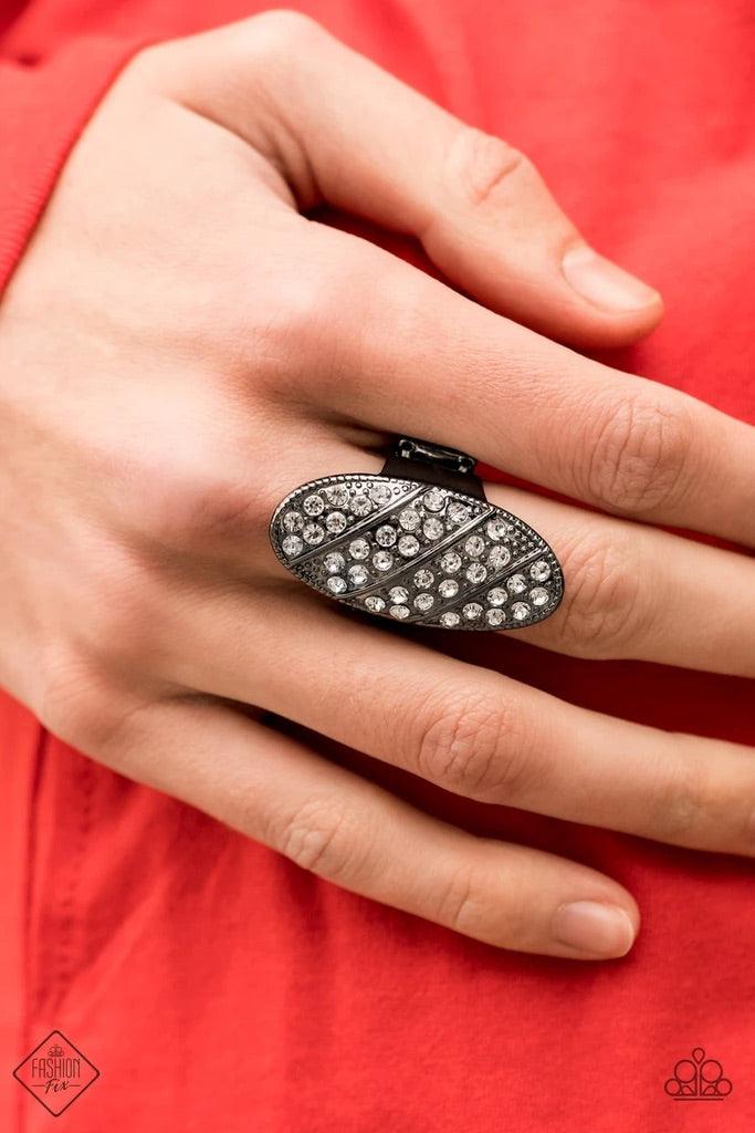 Paparazzi Accessories Galactic Glitz - Black Rows of glassy white rhinestones slant across a stretched oval frame dotted in gunmetal studs, creating a dramatic centerpiece atop the finger. Features a stretchy band for a flexible fit.Sold as one individual