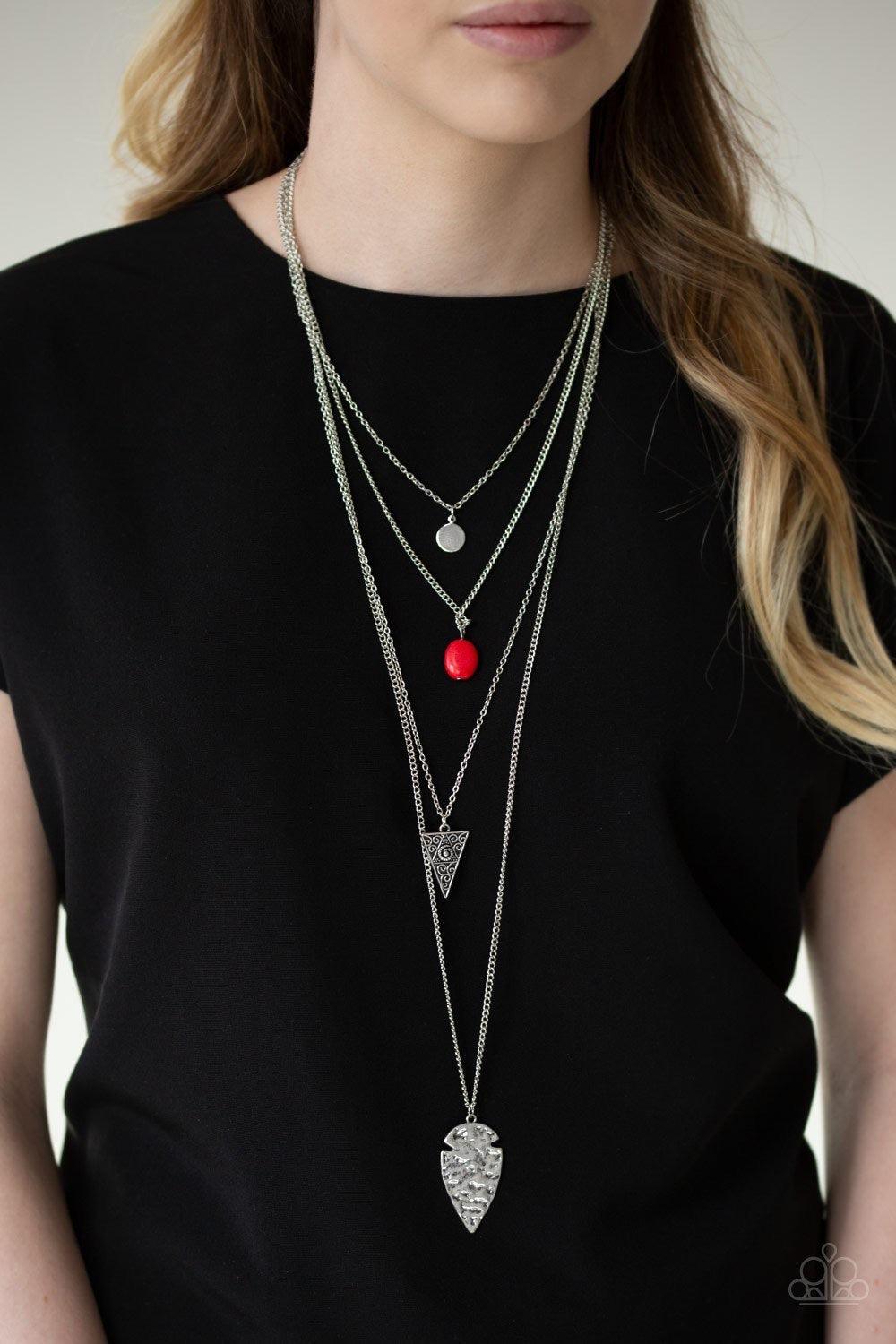 Paparazzi Accessories Grounded in ARTIFACT - Red Glistening silver chains drape across the chest, creating four shimmery layers. A dainty silver disc swings from the uppermost layer above a fiery red stone, ornate triangular frame, and hammered silver arr
