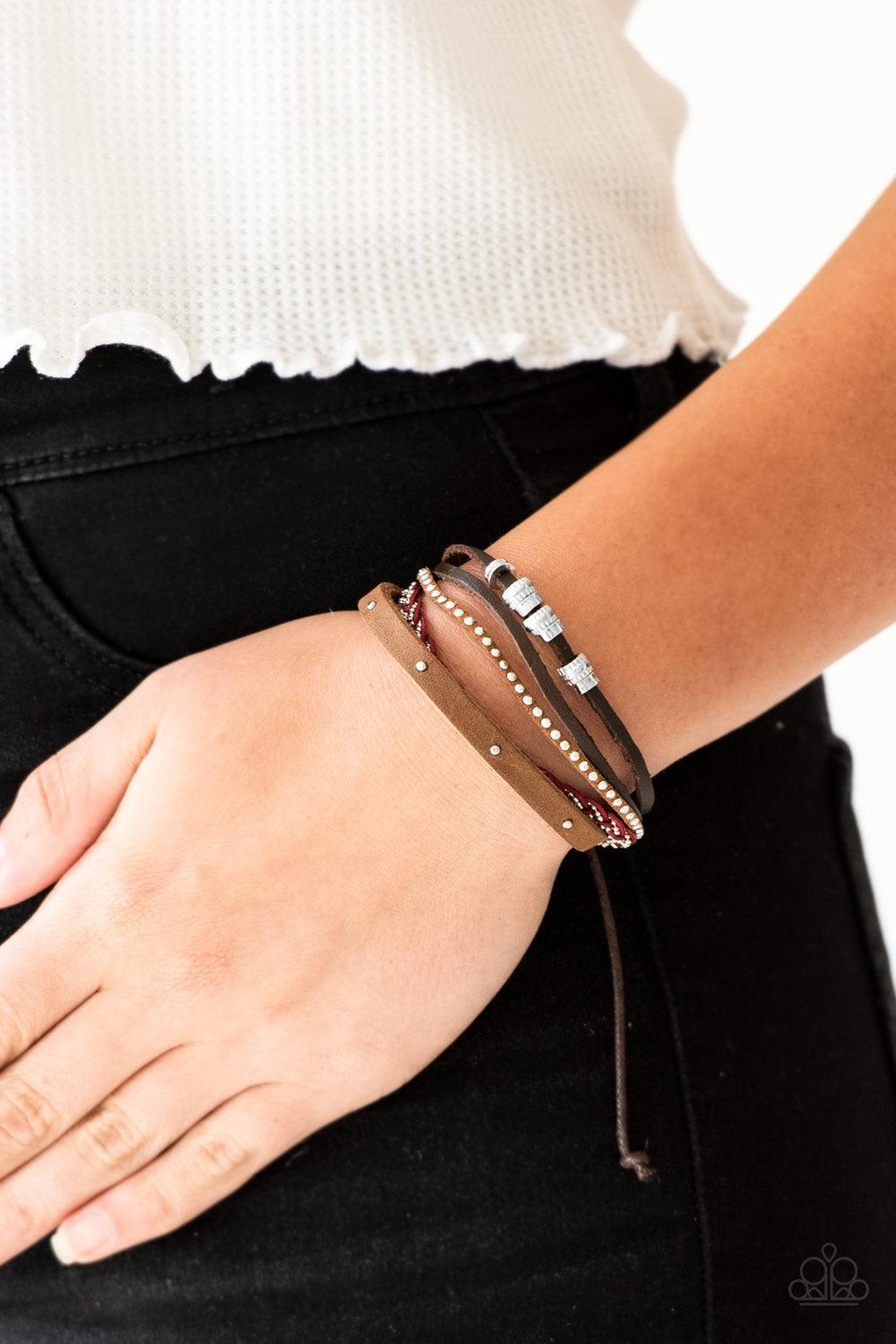 Paparazzi Accessories Day-Trip Trotter - Red Featuring an array of silver accents, mismatched brown leather and suede bands layer across the wrist. Red cording and dainty silver ball chain braid together, adding a refreshing splash of color to the seasona