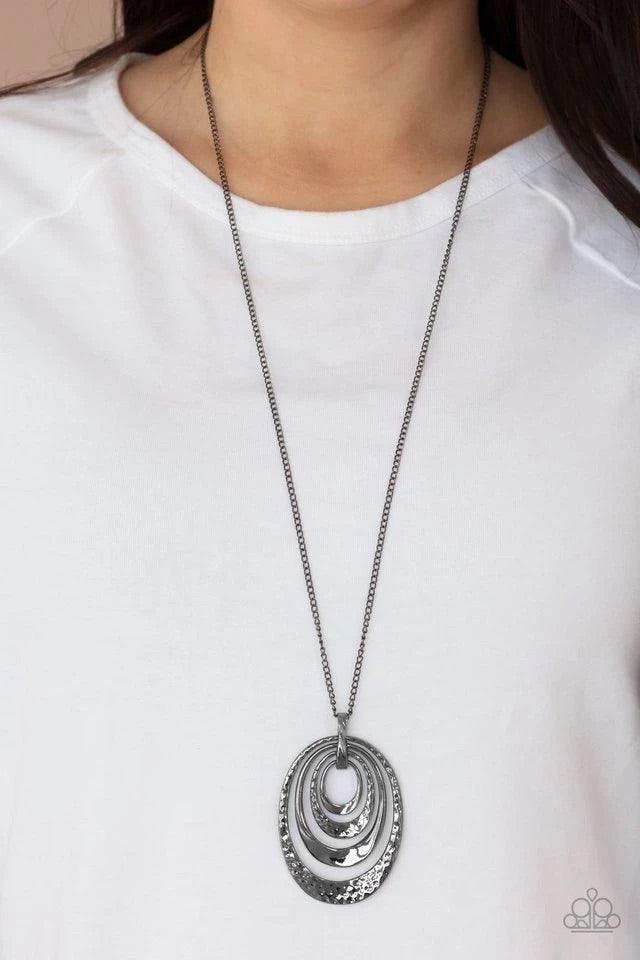 Paparazzi Accessories Renegade Ripples ~Black An asymmetrical collection of plain and hammered gunmetal ovals alternate at the bottom of a lengthened gunmetal chain, creating a dramatically stacked pendant. Features an adjustable clasp closure. Earrings