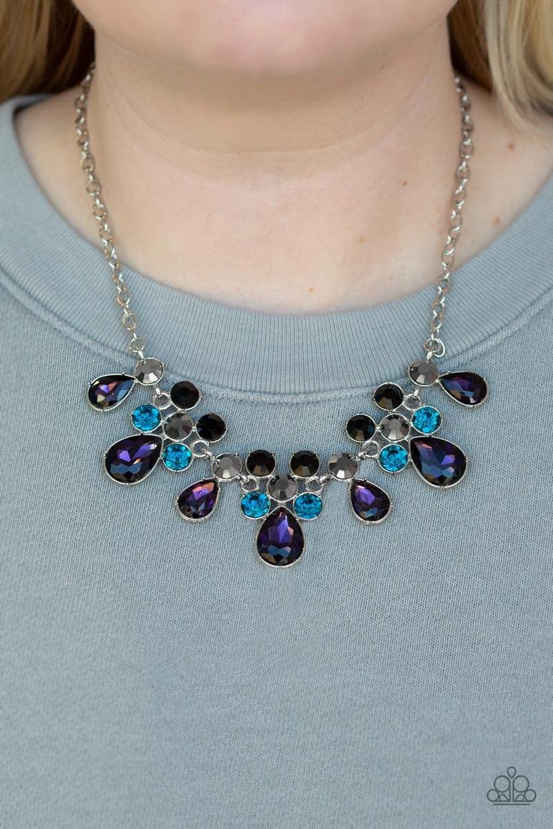 Paparazzi Accessories Debutante Drama - Purple A collection of round and teardrop purple, blue, hematite, and black rhinestones coalesce into dazzling frames as they link below the collar, creating a glamorous fringe. Features an adjustable clasp closure.