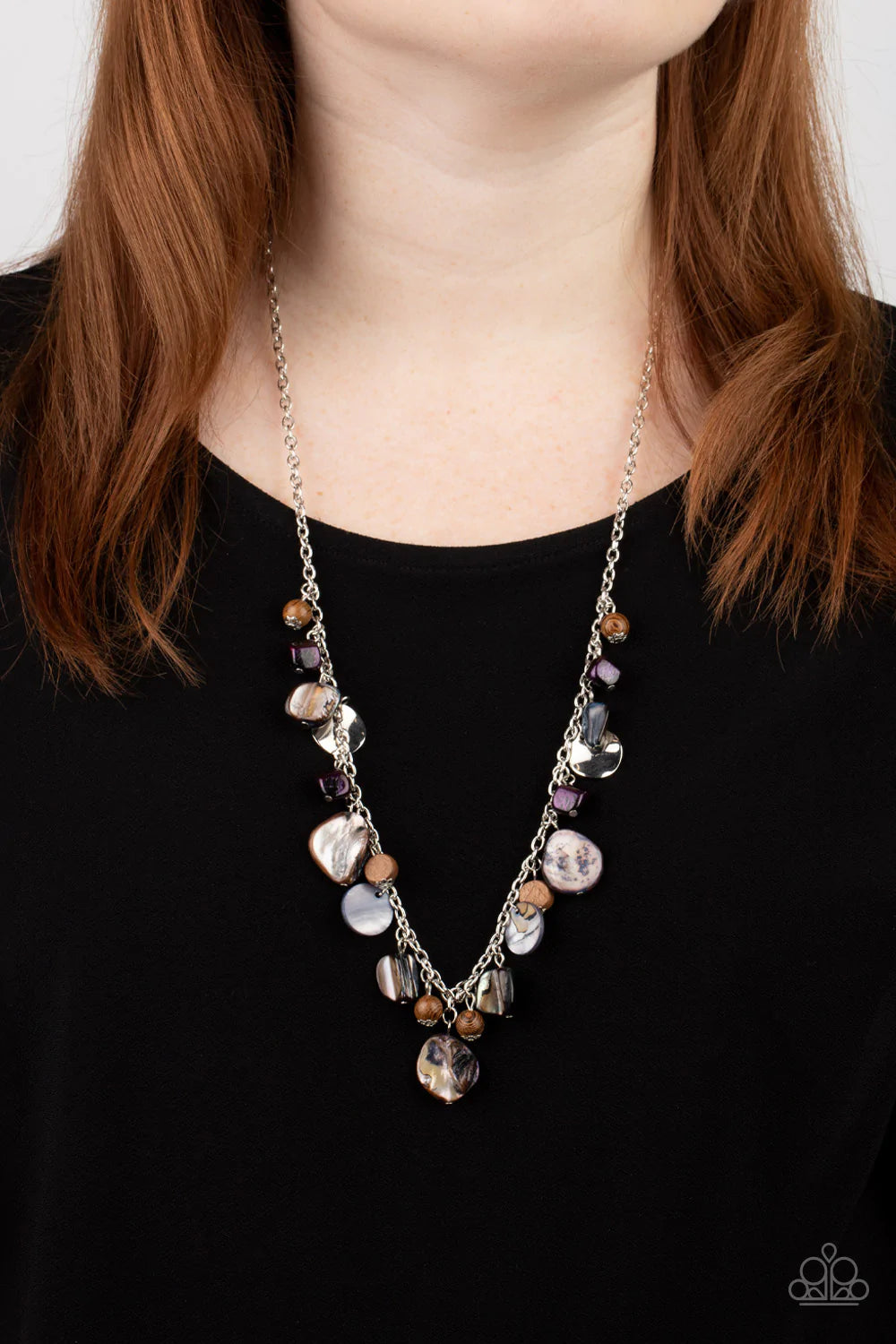 Paparazzi Accessories Caribbean Charisma - Purple A mismatched collection of warped silver discs, brown wooden beads, and iridescent shell-like rock accents dances from the bottom of a classic silver chain, creating a tropical sensation across the chest.