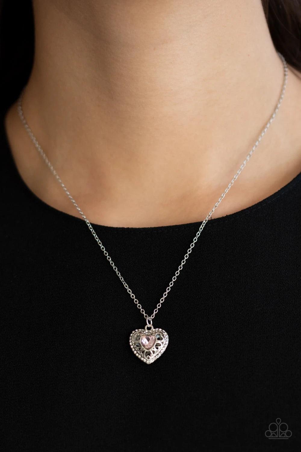 Paparazzi Accessories Treasures of the Heart - Pink Bordered in dainty white rhinestones, an airy silver locket inspired pendant is dotted with a pink heart-shaped rhinestone as it flirtatiously glides along a dainty silver chain below the collar. Feature
