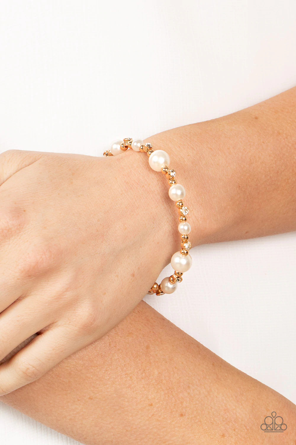 Paparazzi Accessories Chicly Celebrated - Gold A chic collection of white pearls, dainty gold beads, and glassy white rhinestones are threaded along a dainty wire that delicately coils around the wrist for a timeless twist. Sold as one individual bracelet