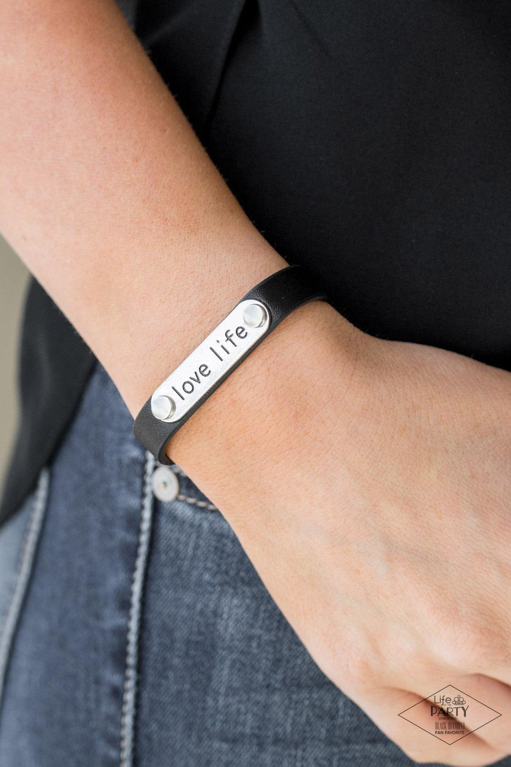 Paparazzi Accessories Love Life - Black A silver plate engraved with the inspirational phrase “love life” is studded in place along a skinny strip of black leather. Brushed in a shiny finish, the dainty band wraps around the wrist in a simply seasonal sty