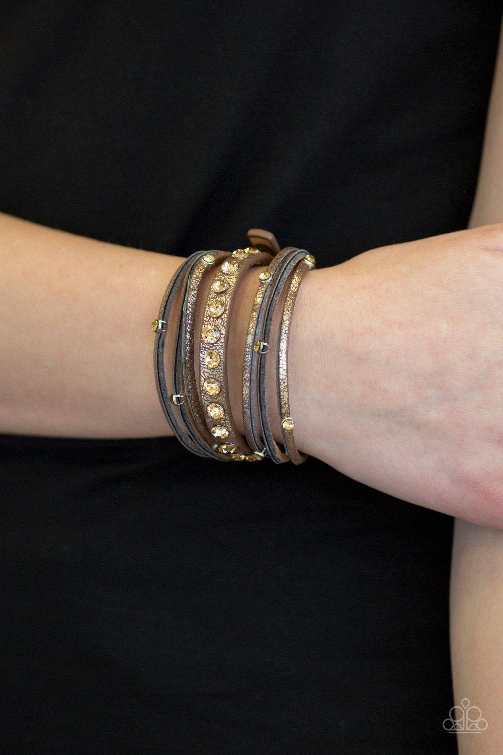 Paparazzi Accessories CATWALK It Off ~Brown Dusted in a golden shimmer, a skinny strip of brown leather is spliced into sections of glittery strands. Infused with golden rhinestones, the elongated band double wraps around the wrist for a fierce one-of-a-k