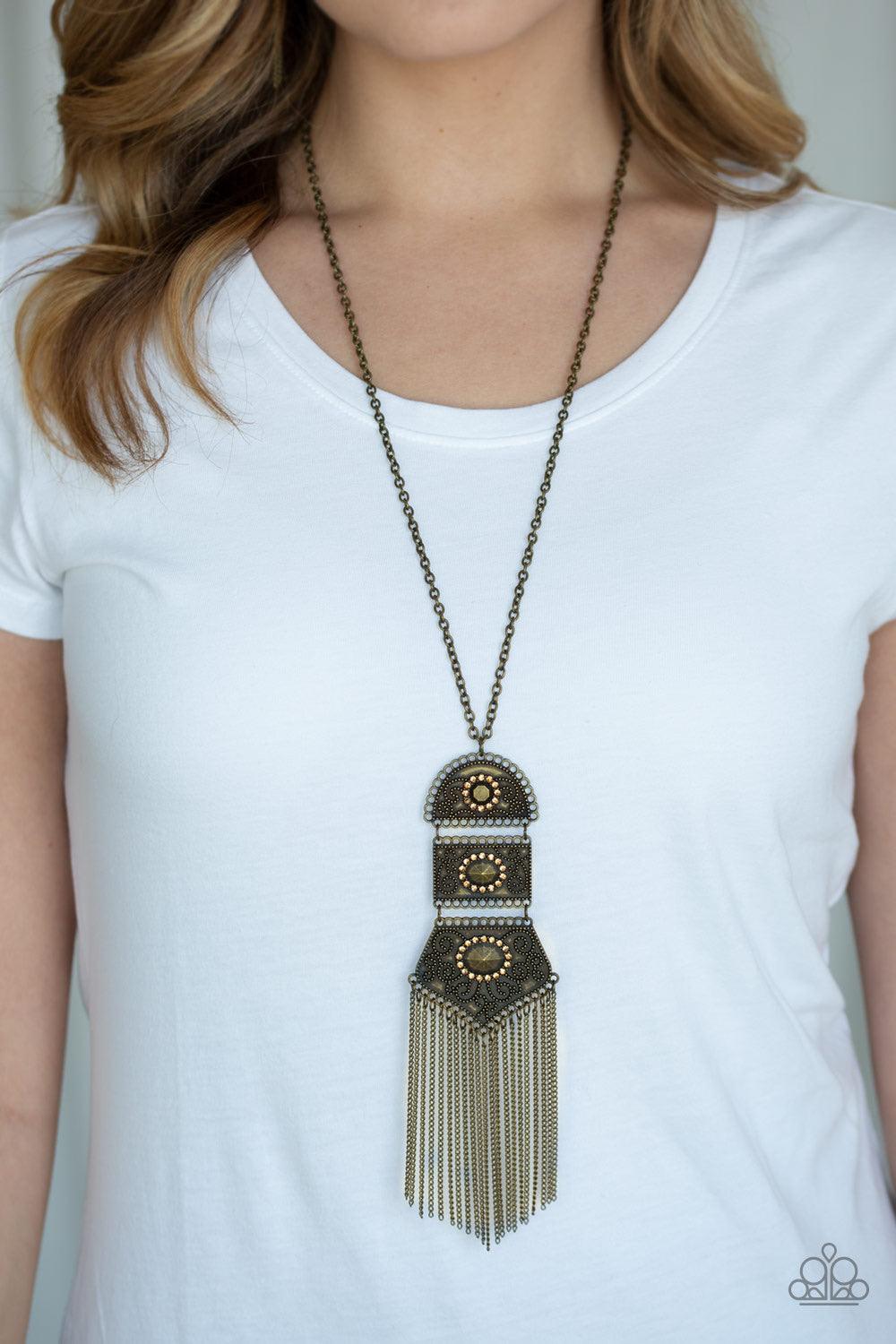 Paparazzi Accessories Tassel Tycoon - Brass Brass beads encircled by topaz rhinestones are nestled inside a row of three vintage frames that cascade down the chest at the bottom of an elongated brass chain. Glistening brass chains stream from the bottom o