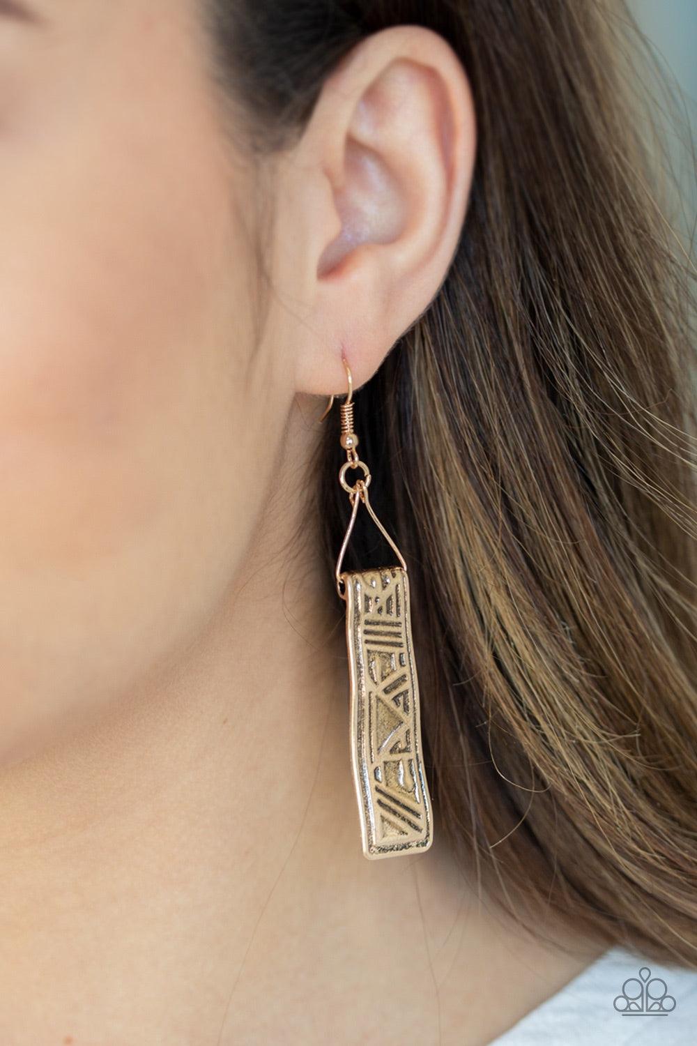 Paparazzi Accessories Ancient Artifacts - Gold Embossed in glyph-like patterns, a hammered gold frame swings from a dainty wire fitting for a tribal inspired finish. Earring attaches to a standard fishhook fitting. Jewelry