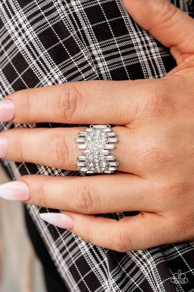 Paparazzi Accessories Urban Empire - White Staggered rows of emerald cut rhinestones flare out from the top and bottom of an explosion of classic white rhinestones, creating a smoldering statement piece atop the finger. Features a stretchy band for a flex