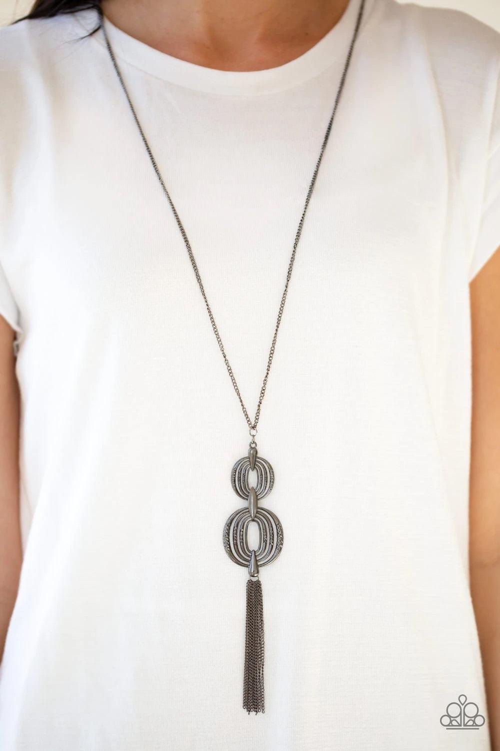 Paparazzi Accessories Timelessly Tasseled - Black Delicately hammered in sections of shimmer, gunmetal circular frames stack into a bold pendant at the bottom of a lengthened gunmetal chain. A shimmery gunmetal tassel swings from the bottom of the stacked