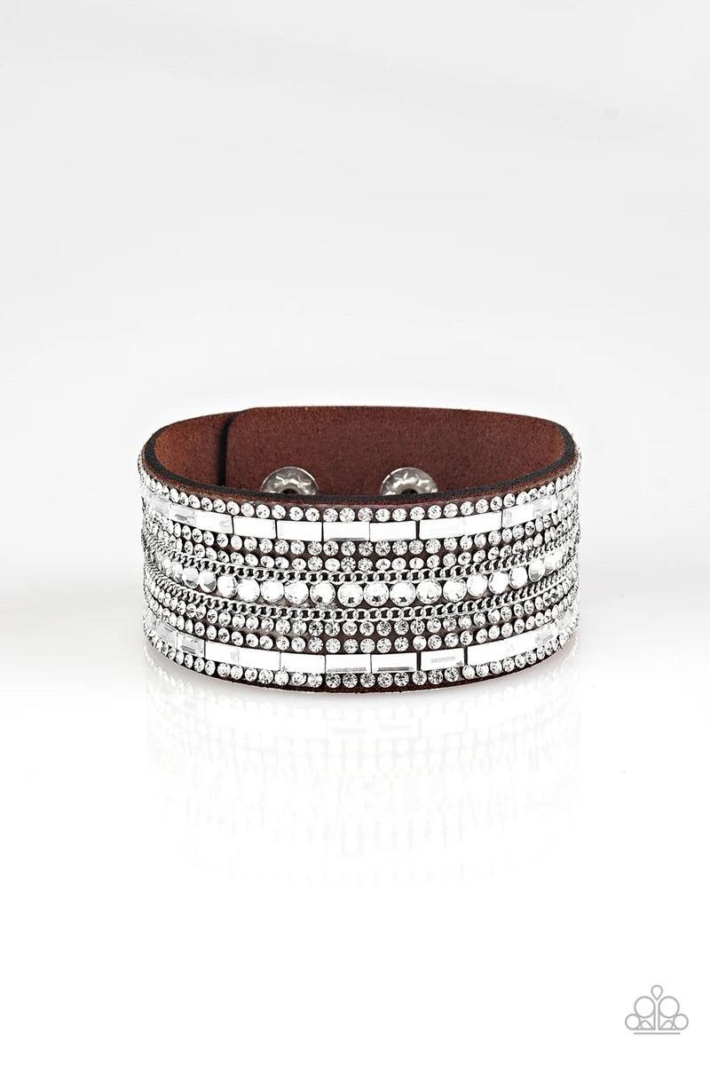Paparazzi Accessories Rebel Radiance - Brown Featuring classic round and edgy emerald style cuts, glittery white rhinestones and glistening silver chains are encrusted along bands of brown suede for a sassy look. Features an adjustable snap closure. Sold
