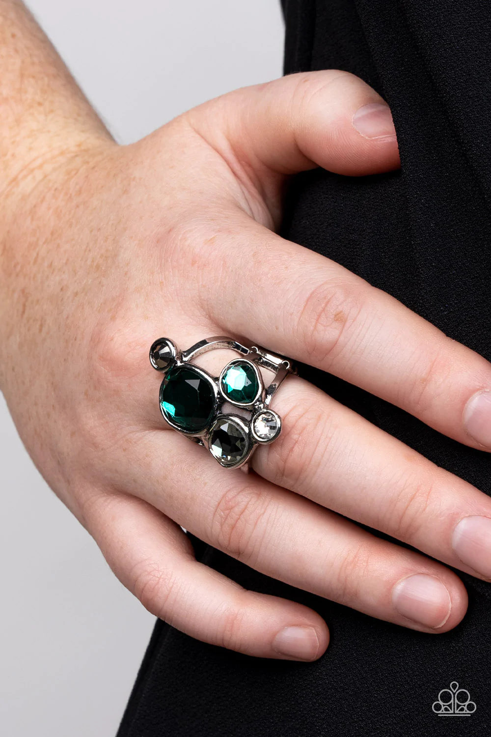 Paparazzi Accessories Demandingly Duchess - Green A collection of sparkling green and smoldering hematite gems in varying sizes, accented by a single white rhinestone, forms an asymmetrical cluster atop the finger. Set in sleek silver frames over airy sil