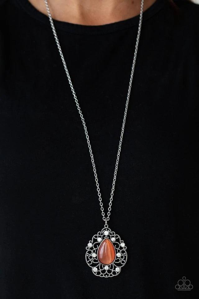 Paparazzi Accessories Bewitched Beam - Orange Glassy white rhinestones dot the front of a studded silver filigree frame that blooms out from a teardrop orange cat's eye stone, creating a bewitching pendant at the bottom of a lengthened silver chain. Featu