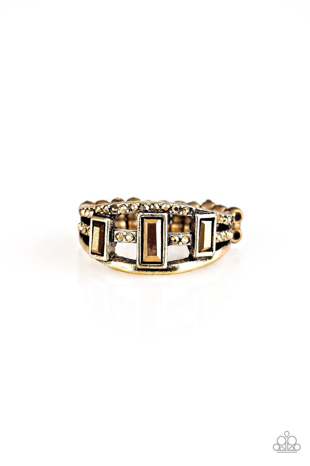 Paparazzi Accessories Noble Nova - Brass Three aurum emerald-cut rhinestones are encrusted along three brass bands radiating with smooth surfaces and sections of glittery aurum rhinestones for an edgy fashion. Features a stretchy band for a flexible fit.