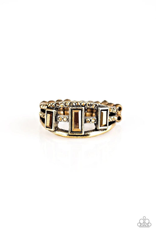 Paparazzi Accessories Noble Nova - Brass Three aurum emerald-cut rhinestones are encrusted along three brass bands radiating with smooth surfaces and sections of glittery aurum rhinestones for an edgy fashion. Features a stretchy band for a flexible fit.