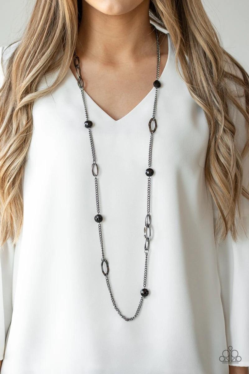 Paparazzi Accessories Duchess Dazzle - Black A collection of black rhinestone gems and abstract gunmetal rings trickle along a classic gunmetal chain across the chest for a refined flair. Features an adjustable clasp closure. Sold as one individual neckla