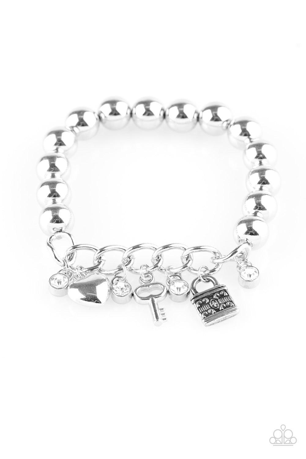 Paparazzi Accessories Feelin Flirtacious - White Attached to a section of silver chain, classic silver beads are threaded along a stretchy elastic band. Glittery white rhinestones, a silver heart, a silver key, and a silver lock swing from the wrist for a