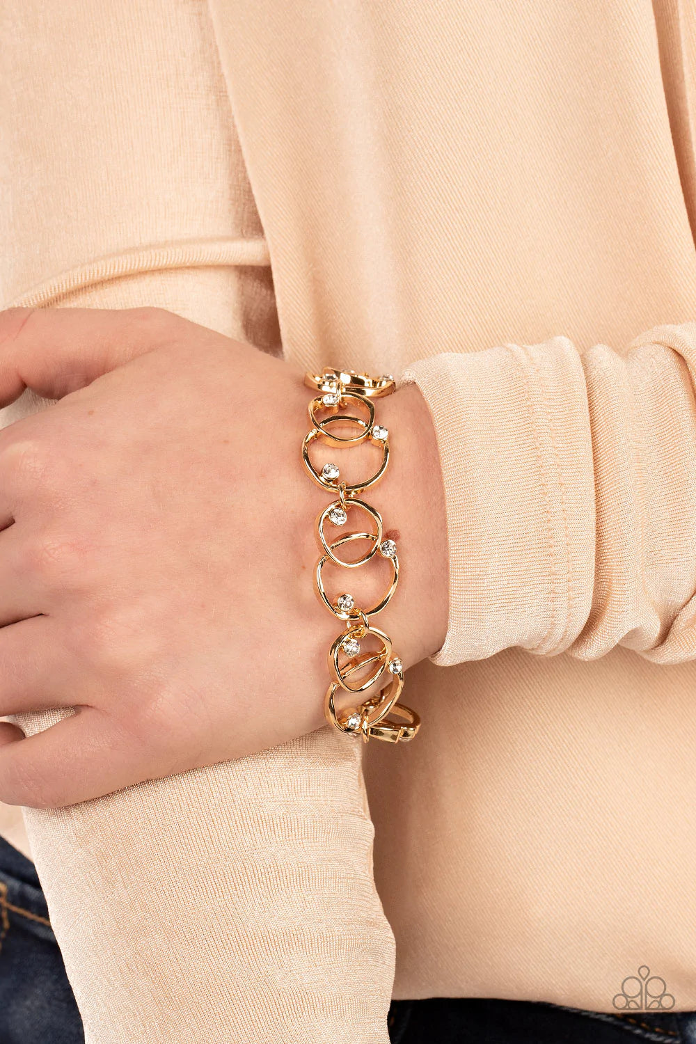 Paparazzi Accessories The Universe Revolves around Me - Gold Sporadically dotted in glassy white rhinestones, asymmetrical pairs of overlapping gold rings delicately link around the wrist for a dizzying display of industrial refinement. Features an adjust