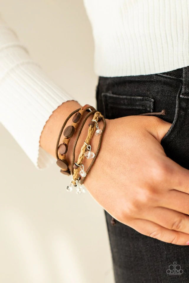 Paparazzi Accessories Run the Rapids - Brown Assorted strands of cording and leather, featuring flat wooden beads and small white polished stones dangling from silver fittings, layer across the wrist for an earthy handcrafted style. Features an adjustable