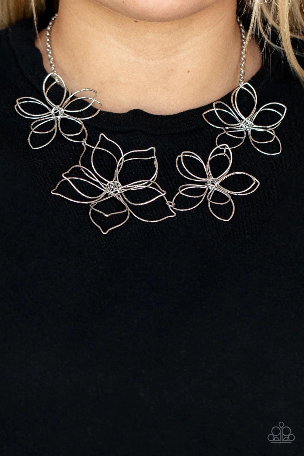 Paparazzi Accessories Flower Garden Fashionista - Silver Shiny silver wire delicately twists into oversized blossoms. Varying in size, the airy floral frames delicately link into an asymmetrical display as the layered frames elegantly pop beneath the coll