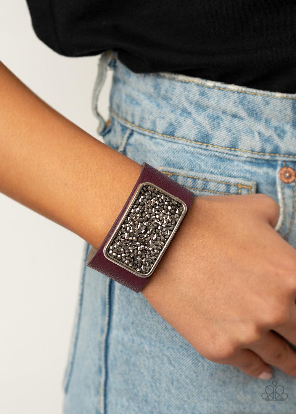 Paparazzi Accessories Interstellar Shimmer - Purple A collision of smoky and hematite rhinestones collect inside a silver rectangular frame that is studded in place in the center of a thick plum leather band, creating a sparkling statement piece around th