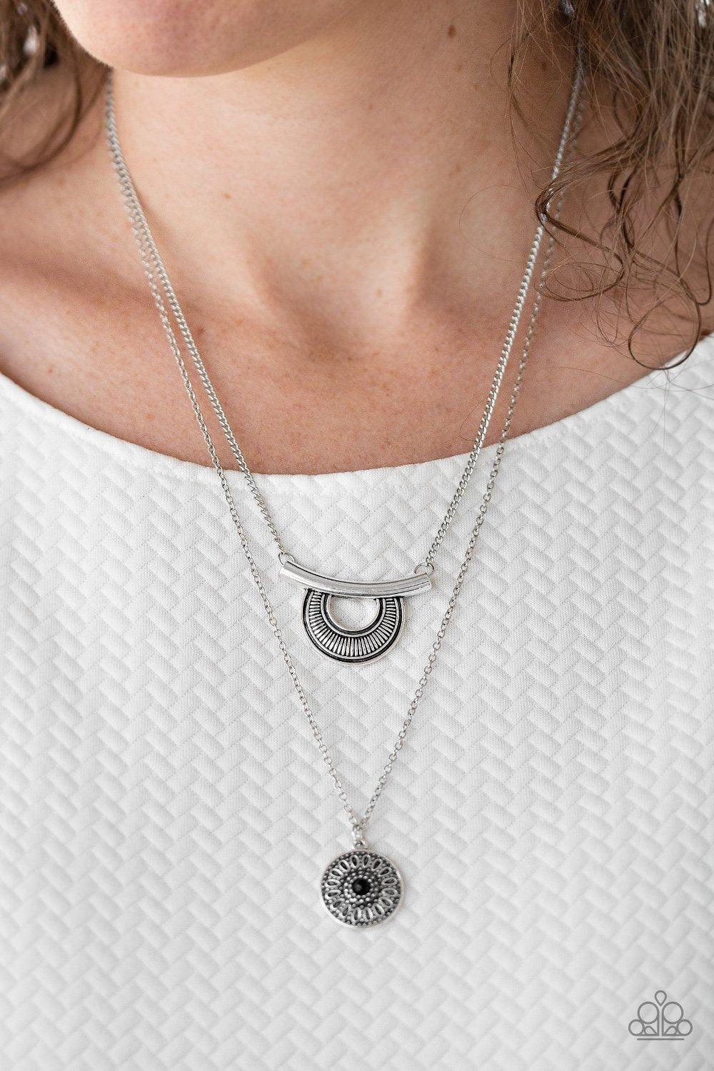 Paparazzi Accessories Gypsy Go-Getter - Black Radiating with linear patterns, a shimmery silver frame swings from the uppermost chain above a silver disc radiating with floral detail. A dainty black bead dots the center of the lowermost pendant for a colo