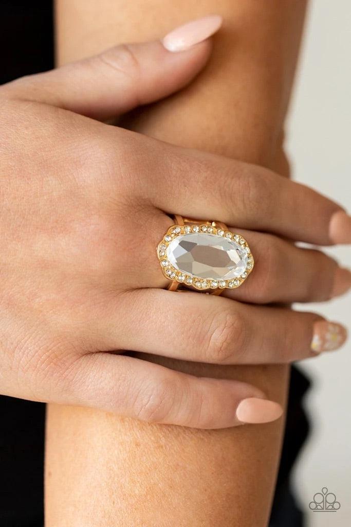 Paparazzi Accessories BLING to Heel! - Gold A dramatically oversized oval white gem adorns the center of a scalloped gold frame dusted in dainty white rhinestones, creating a commanding centerpiece atop the finger. Features a stretchy band for a flexible